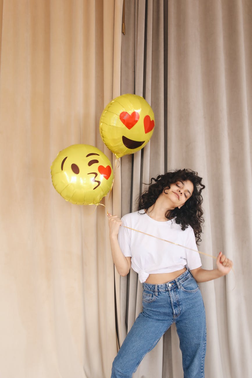 woman in white shirt and blue denim shorts holding yellow and red balloons