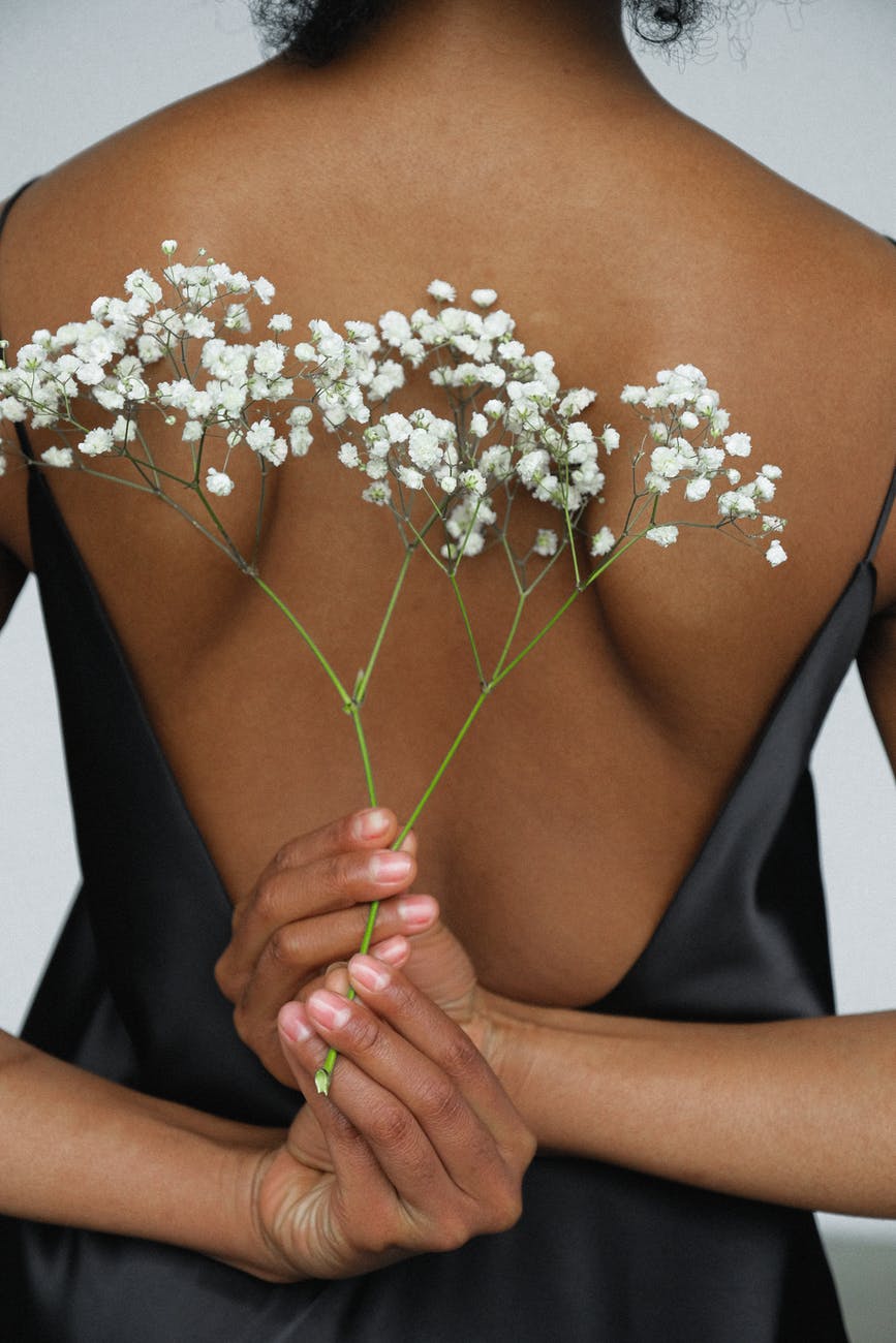 close up photo of woman in black night dress holding white flower behind her back